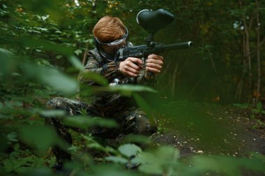 Paintball warrior with gun shoots from the bushes