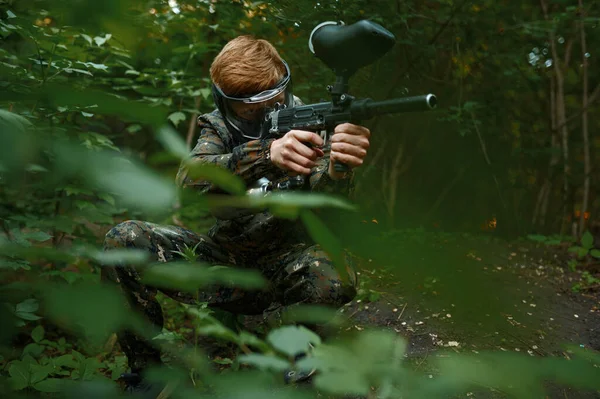 Paintball warrior with gun shoots from the bushes — Stockfoto