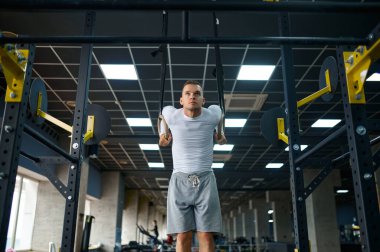 Kaslı adam halkalar üzerinde kas egzersizi yapıyor.