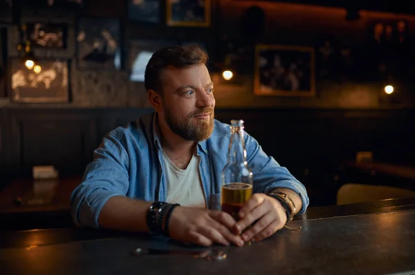 Man with bottle of beer sitting at counter in bar — Stock Photo, Image