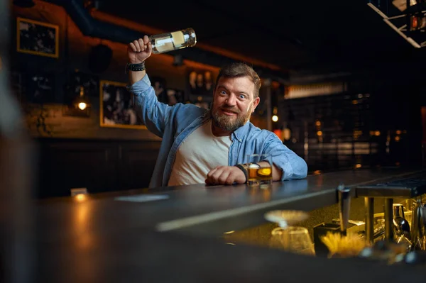Безумный пьяница размахивает бутылкой у стойки в баре — стоковое фото