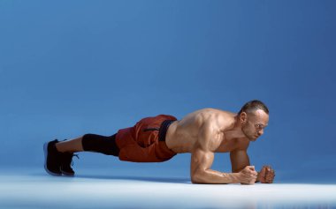 Erkek sporcu dirseklerinin üzerinde durarak karın kaslarını çalıştırır.