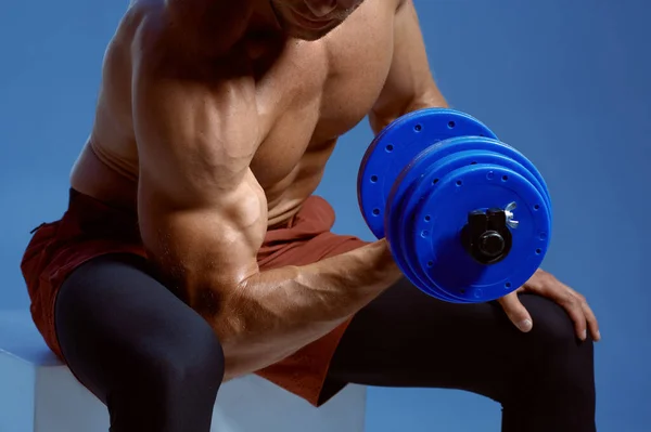 Athlete with dumbbells sitting on cube in studio — Stock Photo, Image