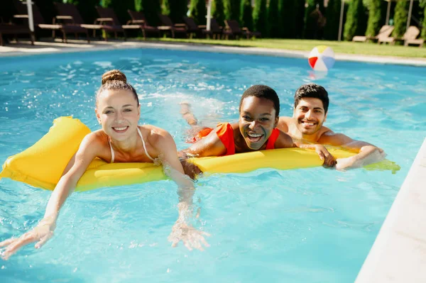 Lächelnde Freunde schwimmen auf einer Matratze im Pool — Stockfoto