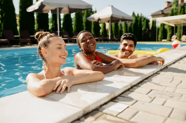 Amigos con bebidas posan al borde de la piscina — Foto de Stock