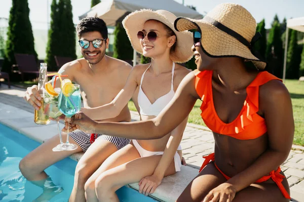 Freunde trinken Getränke am Beckenrand — Stockfoto