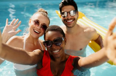 Güneş gözlüklü arkadaşlar havuzda kamera önünde poz veriyorlar.