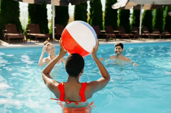 Amigos sorridentes brincam com bola na piscina — Fotografia de Stock