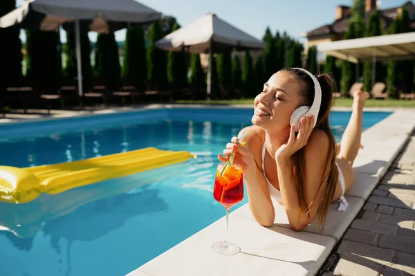 戴耳机的女人在游泳池边喝鸡尾酒 — 图库照片