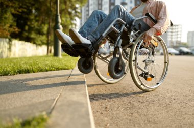 Tekerlekli sandalyedeki engelli adam kaldırımın üstesinden geliyor.