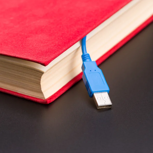 USB-Kabel ragt aus rotem Buch heraus — Stockfoto