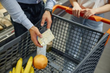 Bir erkek ve bir kadın marketten çeşitli eşyalar alıyorlar, koridorlarda gezinirken ürünleri seçiyorlar.