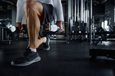 Yaşlı bir adam ve bir kadın dambılları tutarken çömeliyorlar, spor salonunda vücut güçlerine odaklanıyorlar..