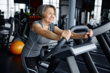 Enerjik üst düzey kadın spor salonunda egzersiz ekipmanlarını güvenle kullanıyor, sağlık ve sağlık hizmetlerini destekliyor.