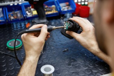 Bir adam, tamir ve bağlantı kurmak için küçük bir elektronik teçhizat parçasında lehim demiri dikkatlice kullanıyor.