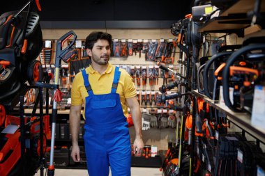 Bahçe aletleri ve aletleri üzerine uzmanlaşmış bir perakende mağazasından çim biçme makinesi seçen bir adam.