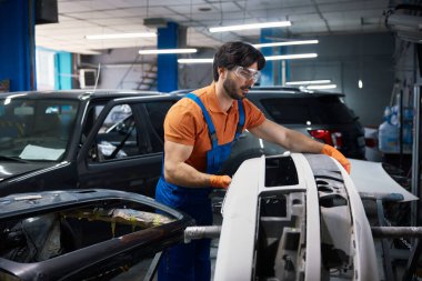 Gülümseyen otomotiv teknisyeni araba tamponu tutuyor, tamirat ve kaportacılık hizmeti sunuyor..