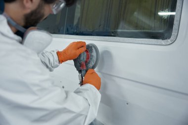 Teknisyen, eldiven, solunum cihazı ve gözlük takıp arabayı zımparalarken...