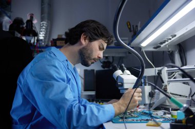 A skilled technician works diligently on complex electronic equipment using precision tools and techniques. Young man is working at his laboratory