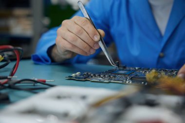 Bir birey, lehimleme demiri kullanarak bir ana kartı dikkatlice onarıyor ve cihazlarda bulunan hassas elektronik bileşenleri kullanmada yeteneklerini gösteriyor.