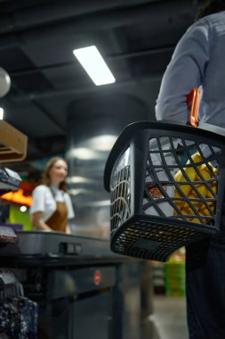 Telaşlı bir markette ağzına kadar dolu bir alışveriş sepeti taşıyan bir adamın yakın çekimi.