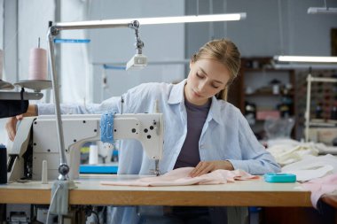 Genç bir terzi, geniş bir stüdyoda kumaş yaratma sanatını sergilemek için bir çalışma istasyonunda özenle kumaş dikiyor..