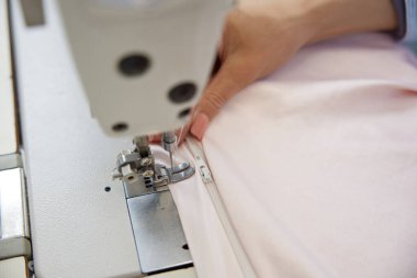 Dikiş makinesi kullanarak kumaşa fermuar dikmek için bir elin detaylı yakın çekimi. Giysi yapımındaki hassasiyet ve beceri.