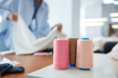 Craftsperson, parlak ışıklandırılmış dikiş atölyesindeki tekstil ve aksesuarları özenle düzenliyor. Parlak stüdyoda terzilik malzemeleri. Dikiş makaralarının yakın plan çekimleri ve terzi çalışıyor