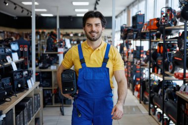 Kaynakçı işçi mavi tulumlu bir kaynak makinesini bir mağazanın içinde tutuyor, araştırıyor ya da işini yapmaya hazırlanıyor.