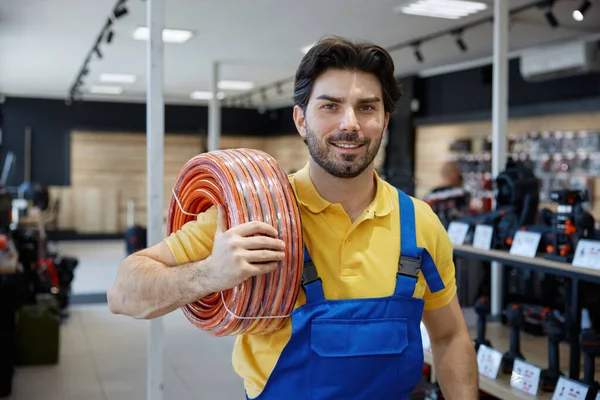 Mavi tulumla birlikte parlak sarı bir gömlek giyen bir adam elinde bir hortum tutuyor ve bir görev üzerinde çalışmaya hazır.