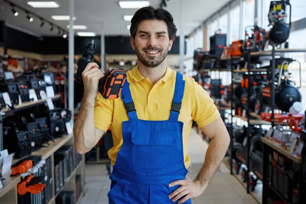 İşçi elinde matkap varken bir mağazada duruyor, satılık araçları gösteriyor