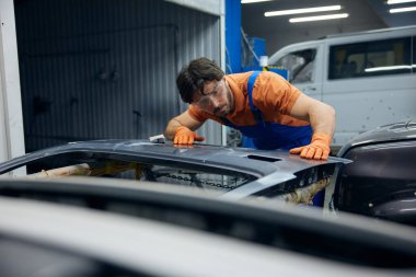 Profesyonel atölye, eldiven takan bir tamirci özenle kumla kaplanmış ve arabanın kapı panelini inceliyor.