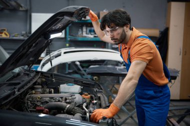 Üniformalı tamirci, garaj atölyesindeki motor motorunu inceliyor. Teşhis, onarım ve bakım..