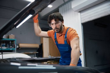 Üniformalı tamirci, garaj atölyesindeki motor motorunu inceliyor. Teşhis, onarım ve bakım..