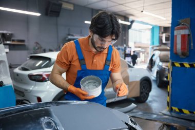 Otomobil teknisyeni, garaj atölyesinde astar ve maskeli bir araba paneli hazırlıyor..