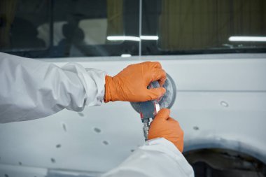 Koruyucu giysili teknisyen ve eldiven zımparalama araç paneli. Yörüngesel zımpara makinesi, boya için yüzeyi hazırlıyor. Elinde zımpara malzemesi olan yetenekli bir işçi.