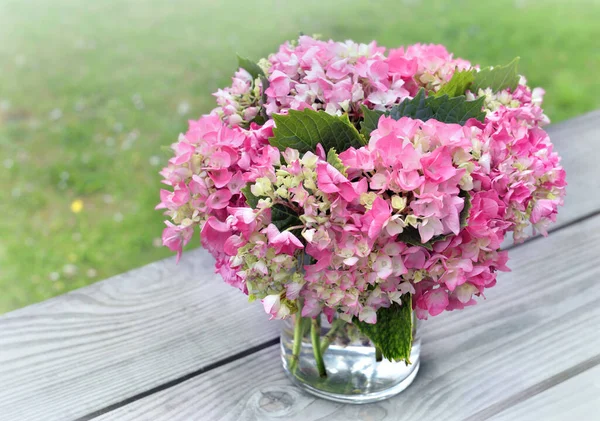 romantic round bouquet of pink hydrangea in a glass vase put on a table in garden