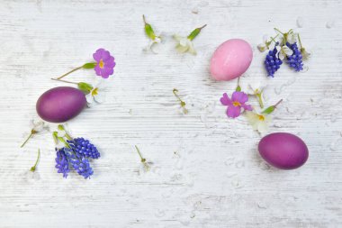 Pembe ve mor renkte boyanmış paskalya yumurtaları bahar çiçekleri ve taç yaprakları arasında bir masada. 