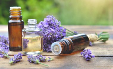 Bahçe bahçesindeki ahşap bir masaya yerleştirilmiş yağ şişeleri ve lavanta çiçeği.