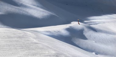 Taze karla kaplı ve narin gölgelerin üzerinde pırıl pırıl kar yağışı Alp kayak merkezinin karlı dağlarında kayak pistinde. 