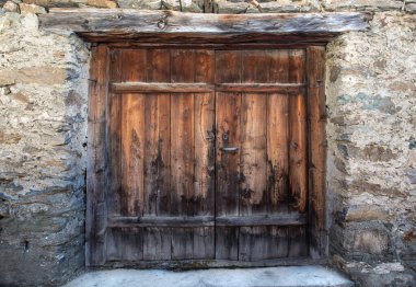 front view on the old wooden door of a traditional alpine rustic chalet with stoned wall 