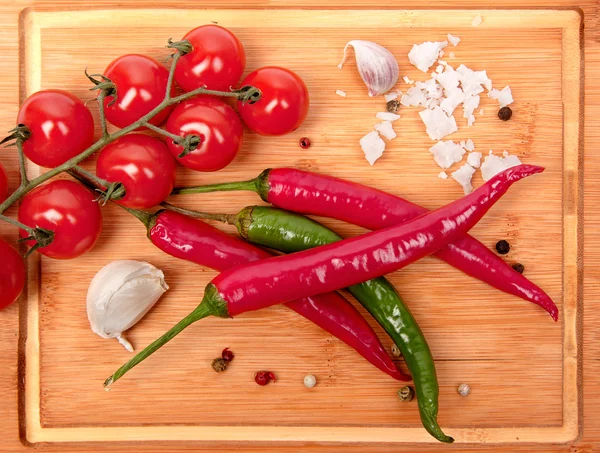 Red chili pepper, tomato and garlic on a wooden board — Stock Photo, Image