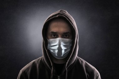 Karanlıkta Coronavirus 'a karşı koruyucu maske takan kapüşonlu adam.