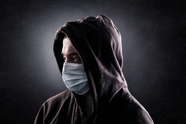 フード付きの男身に着けています保護顔マスクに対してコロナウイルスで暗闇の中 — ストック写真