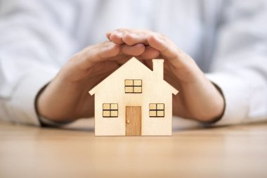 Tahta oyuncak ev ellerle korunuyor. Ev sigortası kavramı