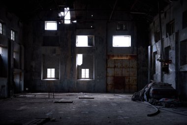 Terk edilmiş endüstriyel fon. Beton duvarlı eski karanlık depo, paslı kapı ve kırık pencereden süzülen ışık.