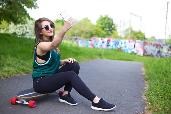 Девушка со скейтборда в парке делает селфи — стоковое фото