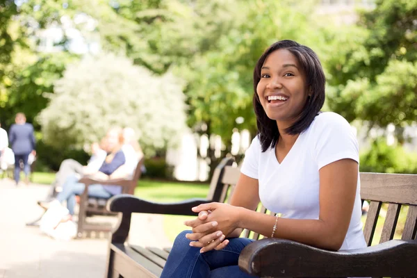 Feliz jovem mulher sentada em um banco de parque — Fotografia de Stock