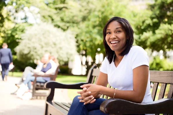 Happy young woman sitting on a park bench — Stock Photo, Image