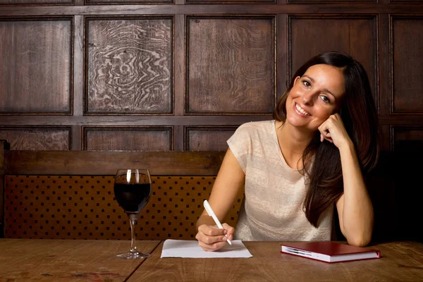 Mujer joven disfrutando de una copa de vino y escribiendo una carta — Foto de Stock